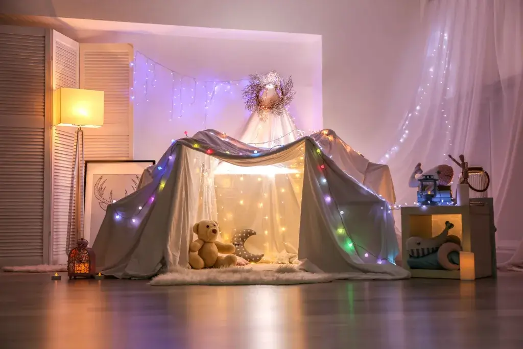 Living room blanket fort with twinkly lights and stuffed animals.