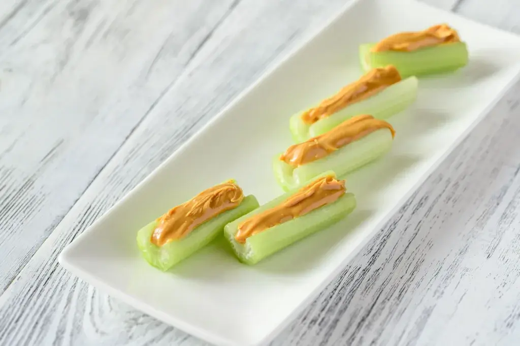 Celery and peanut butter sticks on a white platter.