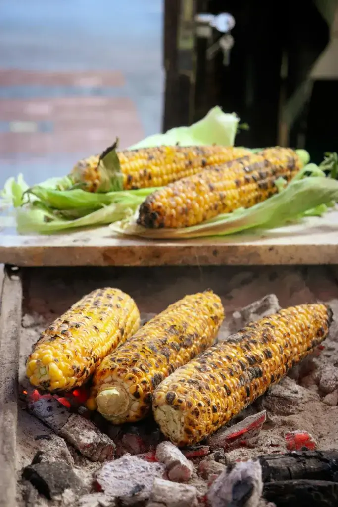 Delicious grilled corn on the cob over hot charcoal, perfect for summer BBQs and outdoor gatherings.