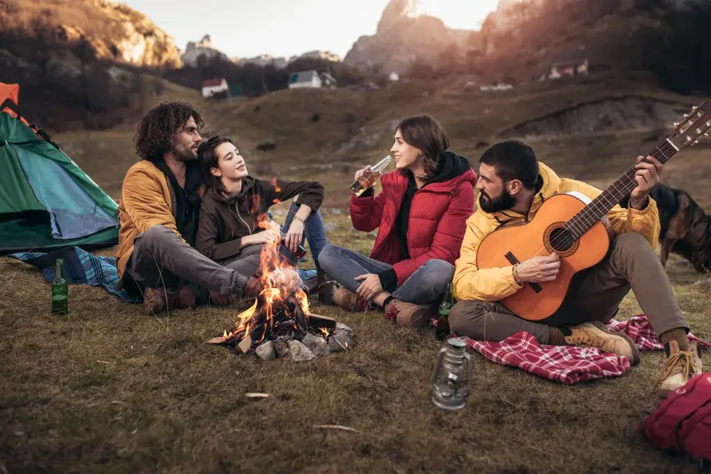 Group of friends sitting around a campfire smiling and playing a guital.