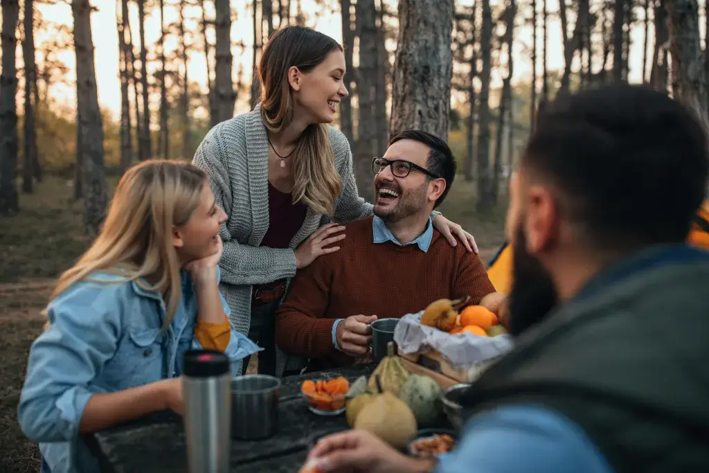 Group of friends fall camping sitting at a picnic table and laughing.