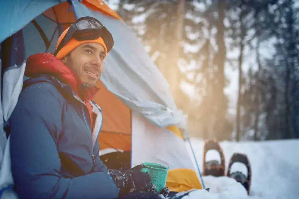 Man sitting next to a tent in the snow after a day of snowshoeing.