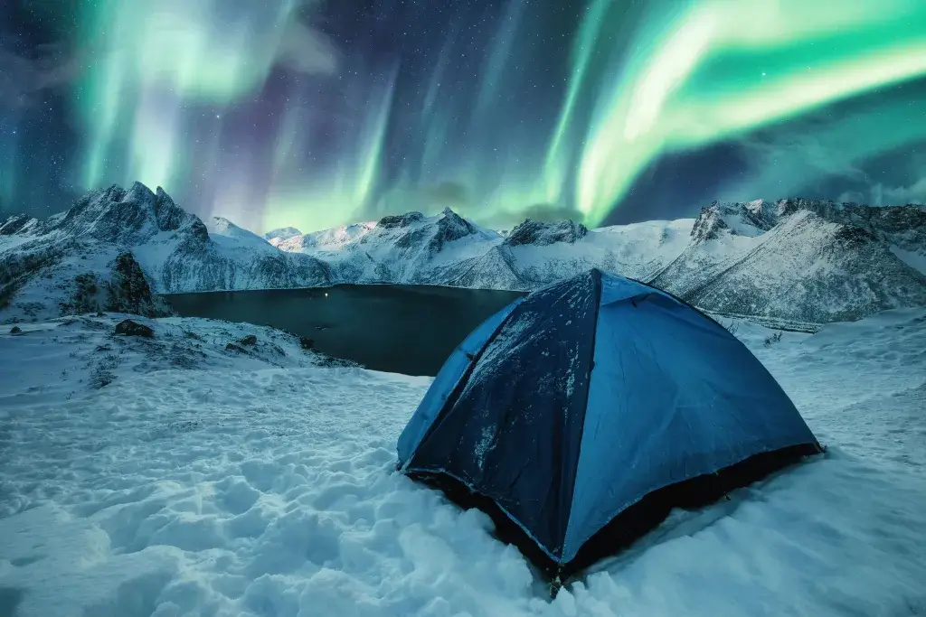 Tent in the snow next to a lake with Northern Lights in the background.
