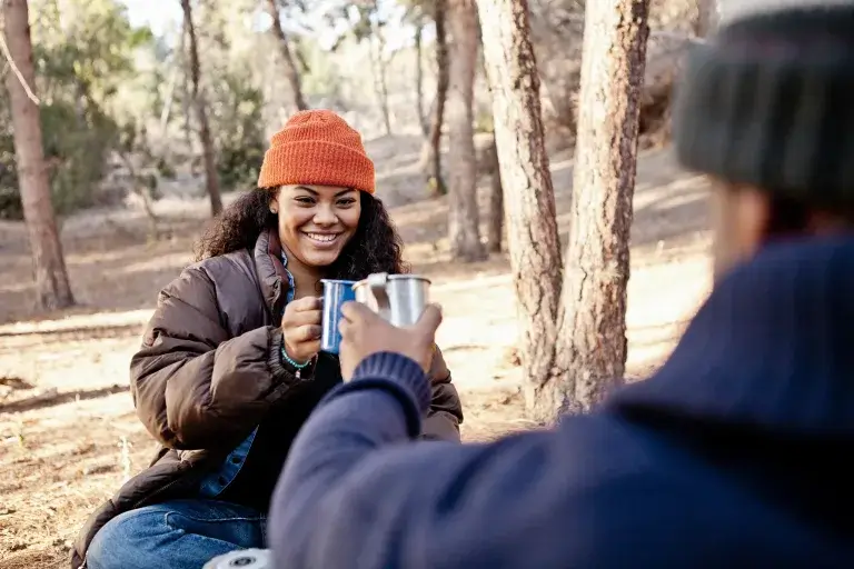 Man and woman drinking a hot drink at a campsite during fall.