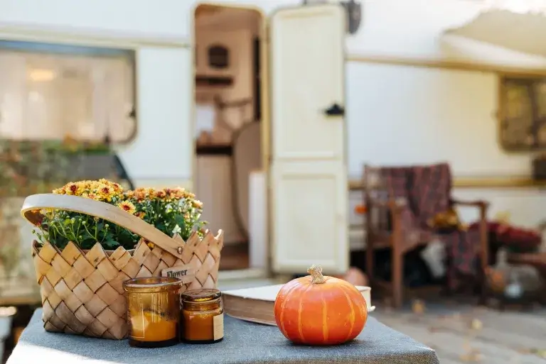 RV in the background and a picnic table with a mini pumpkin, scented candles and a basket with flowers.
