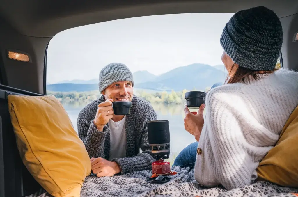Man and woman drinking hot tea and wearing beanies at camp.