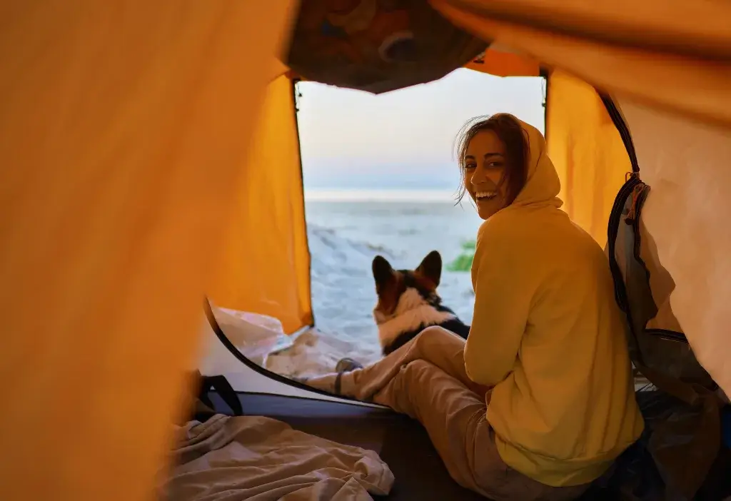 Woman and dog sitting in a tent looking at snow outside.