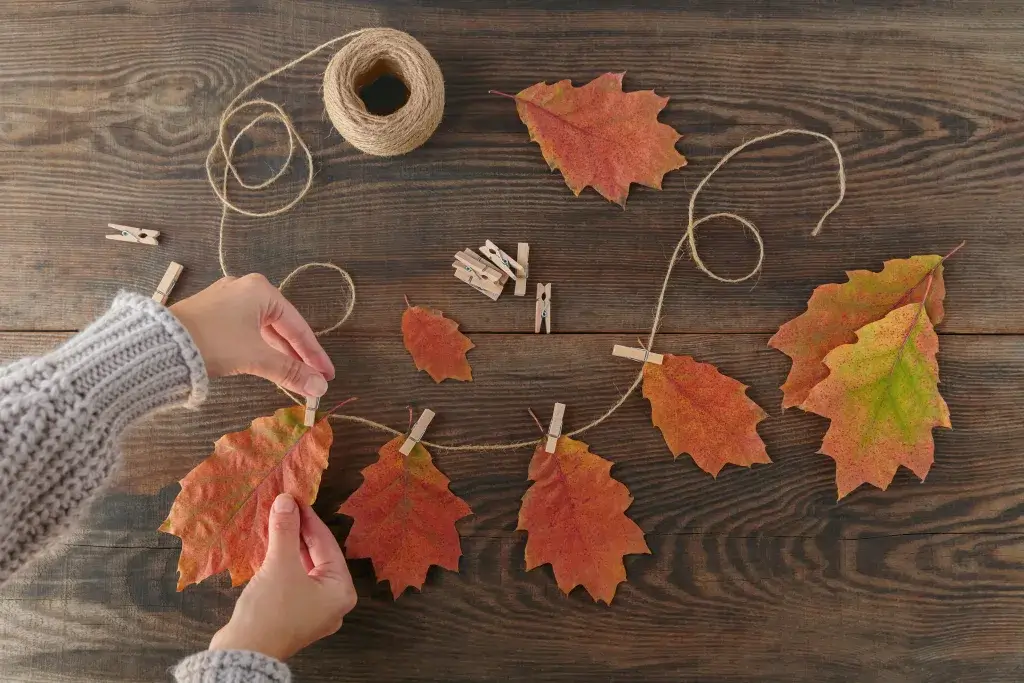 Crafting a garland with twine and colorful fall autumn leaves.