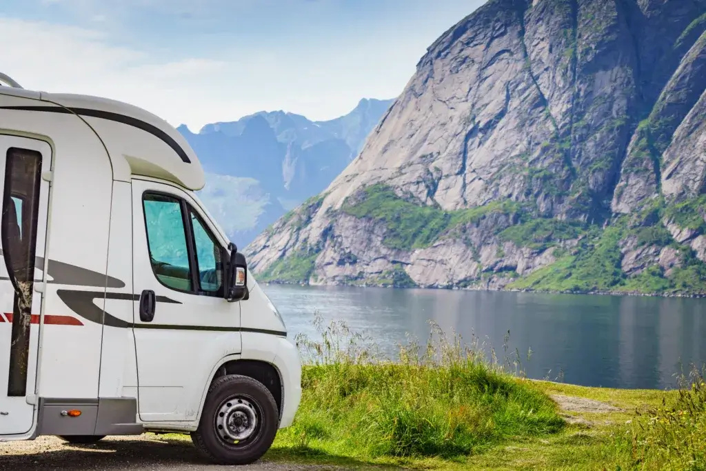 Motorhome parked in front of lake with a large rock in the background.