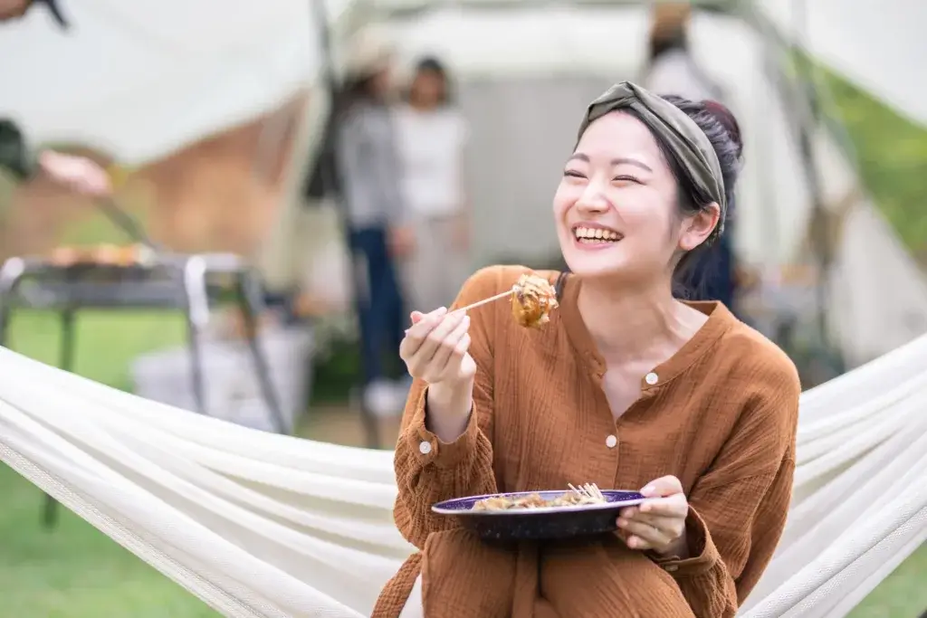 Woman sitting in a hammock smiling and eating a healthy meal.