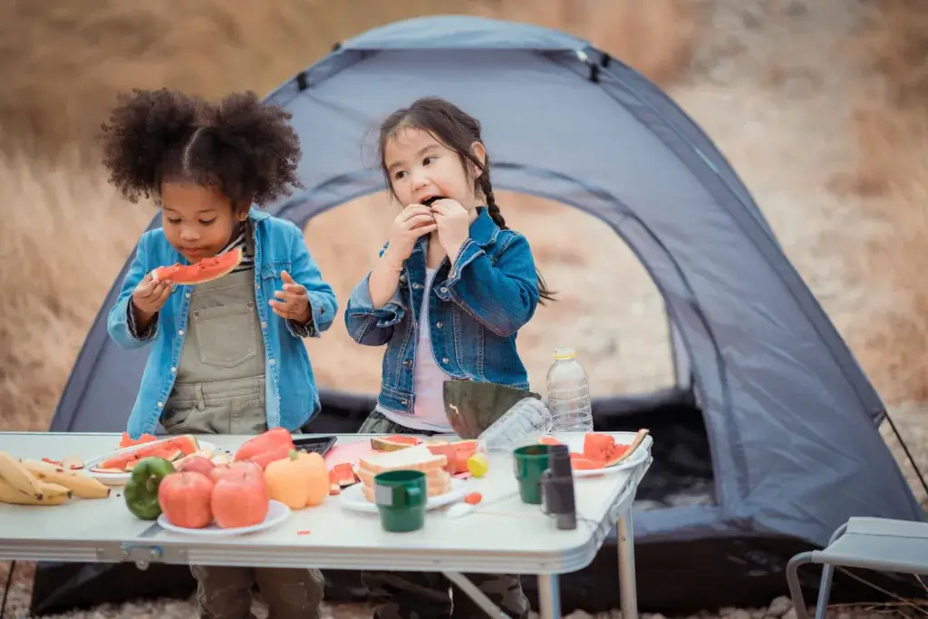 Two young children at camp are eating fresh fruit.