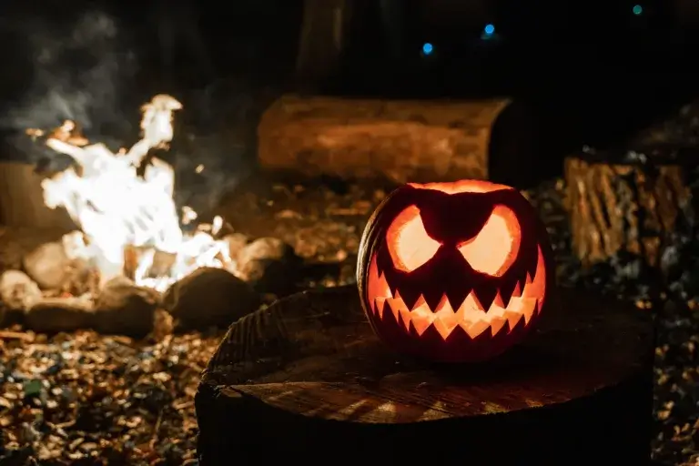 Lit up Halloween Jack O Lantern next to a campfire.