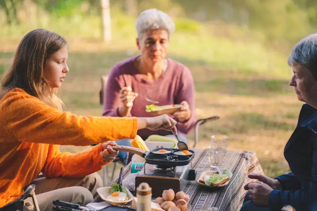 Grandmother and granddaughter cooking and eating a healthy meal at camp.