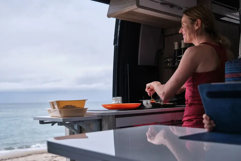 Woman cooking in a camper van with an ocean view.