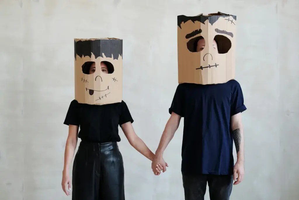 Couple wearing handmade cardboard Halloween masks holding hands.