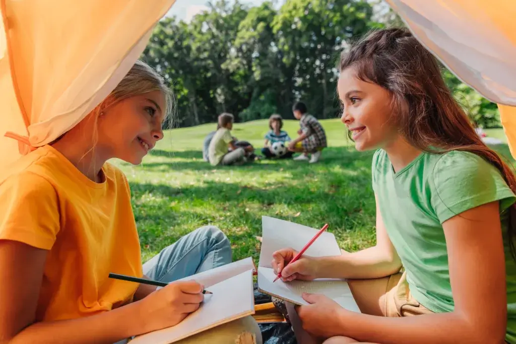 Two young girls are sitting in a tent writing in their journals.