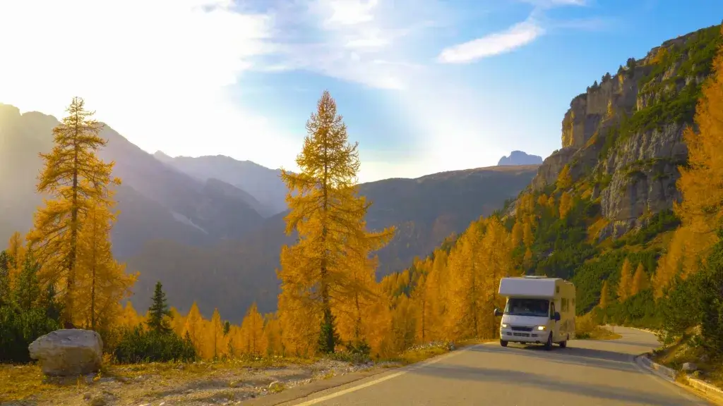 RV motorhome driving down a road with fall autumn colors.