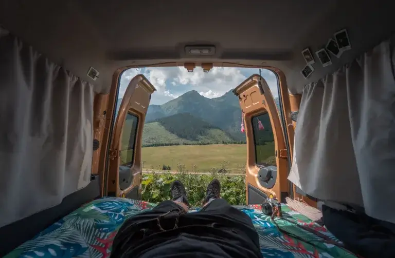 Man lying in bed in a van with the back doors open looking at the mountains.