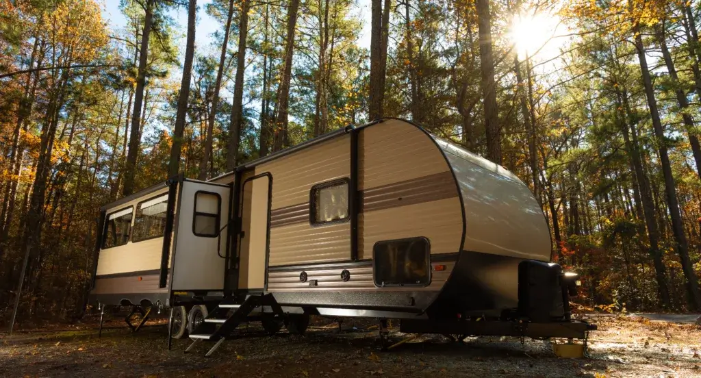 RV trailer parked in a wooded area with fall autumn colors.
