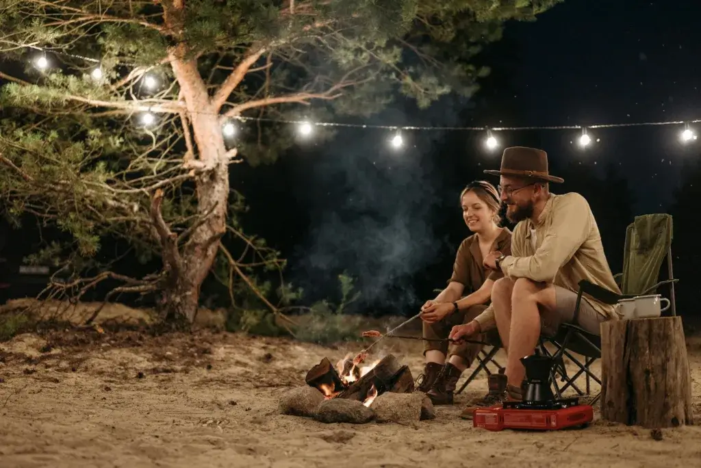 Couple enjoying a cozy camping night by a bonfire under festive lights.