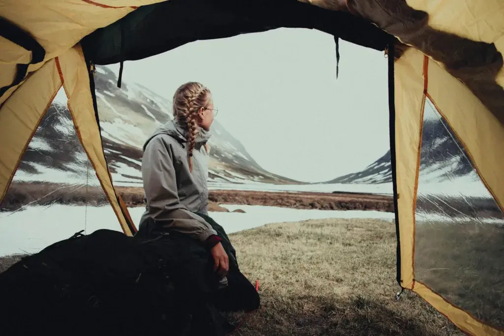 Woman with braids enjoying a serene mountain campsite from her tent, capturing the essence of adventure.