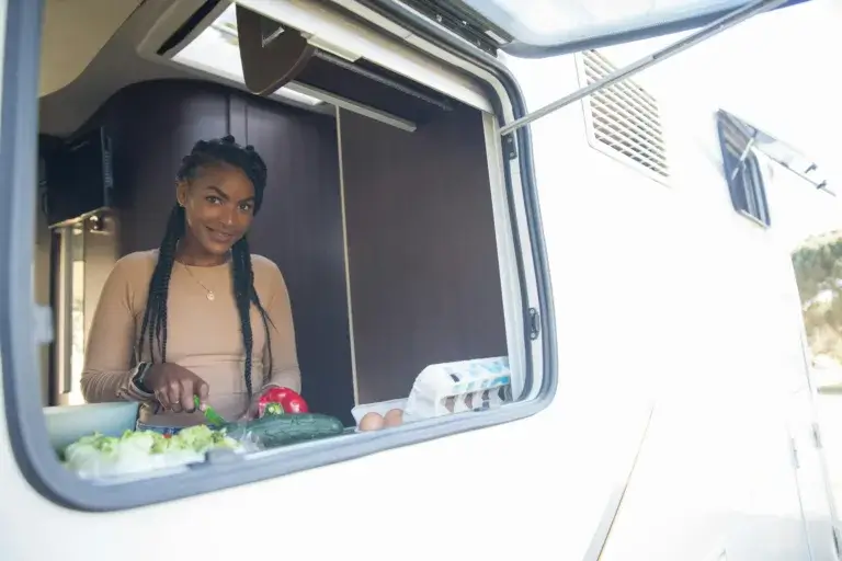 Young woman preparing food with fresh vegetables in a caravan kitchen. Outdoor lifestyle in a cozy mobile home.