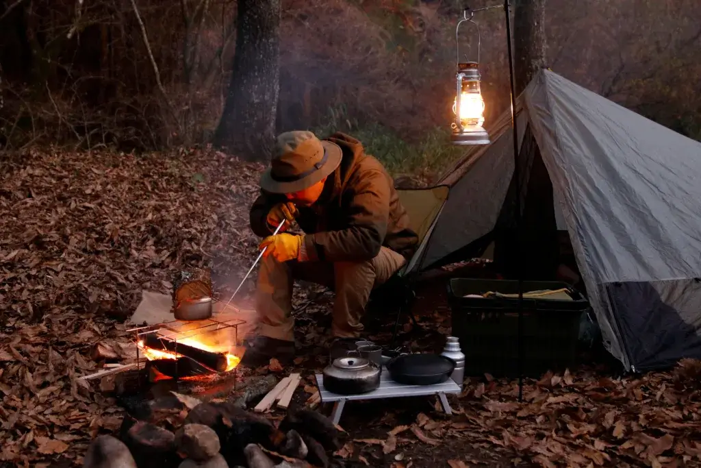 Man sitting next to a tent starting a campfire on a winter evening.