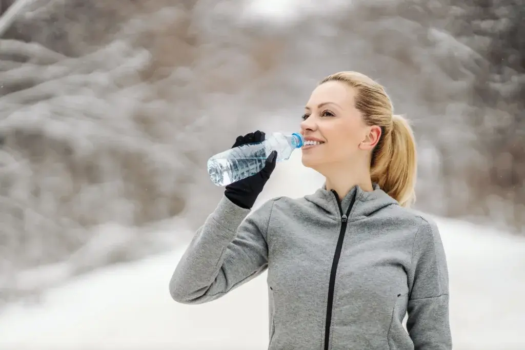 Woman drinking from a water bottle on a cold winter snow day.