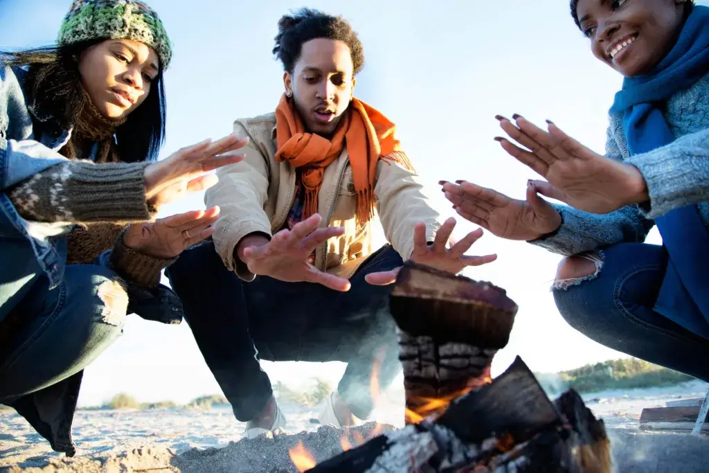Friends warming their hands over a campfire on a snowy winter day.