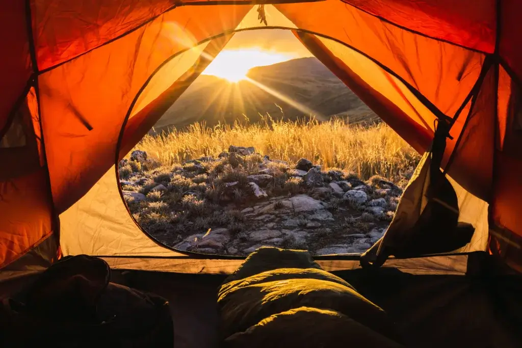 Person in a sleeping bag in a tent on a cold winter morning at sunrise.