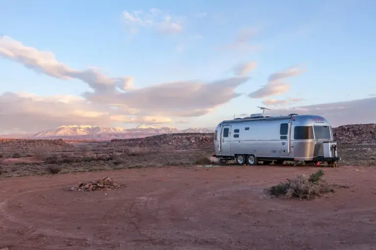 Silver trailer in desert landscape at sunset with mountains in the background.