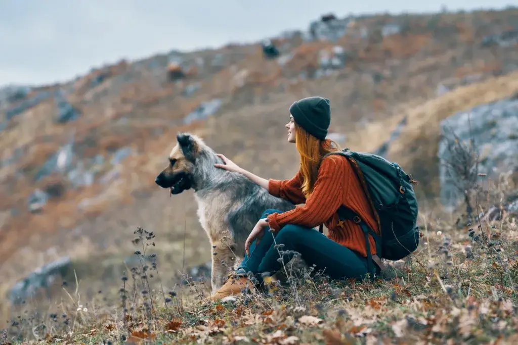 Woman and dog sitting down on a hiking trail looking at the hills.