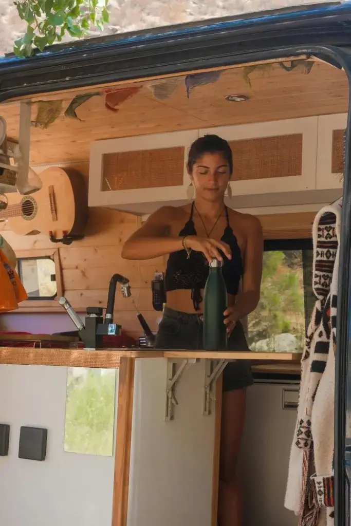 Woman preparing a drink inside a cozy van, showcasing a carefree lifestyle.