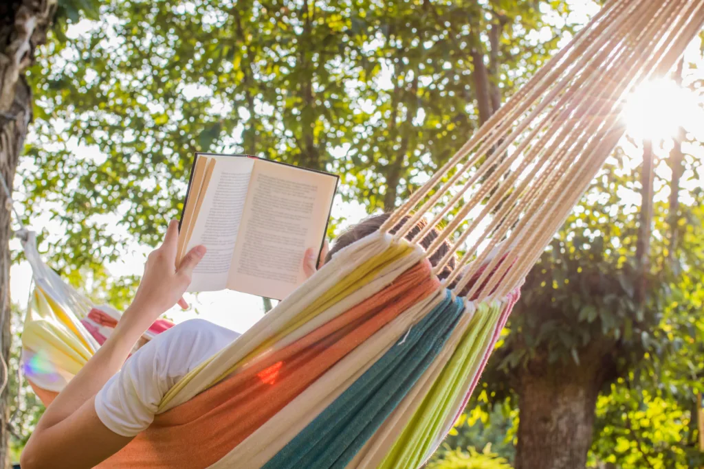A woman lying in a hammock reading a book.