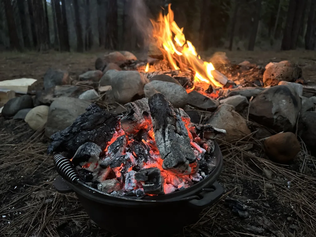 Dutch over sitting next to a campfire with hot coals on top.