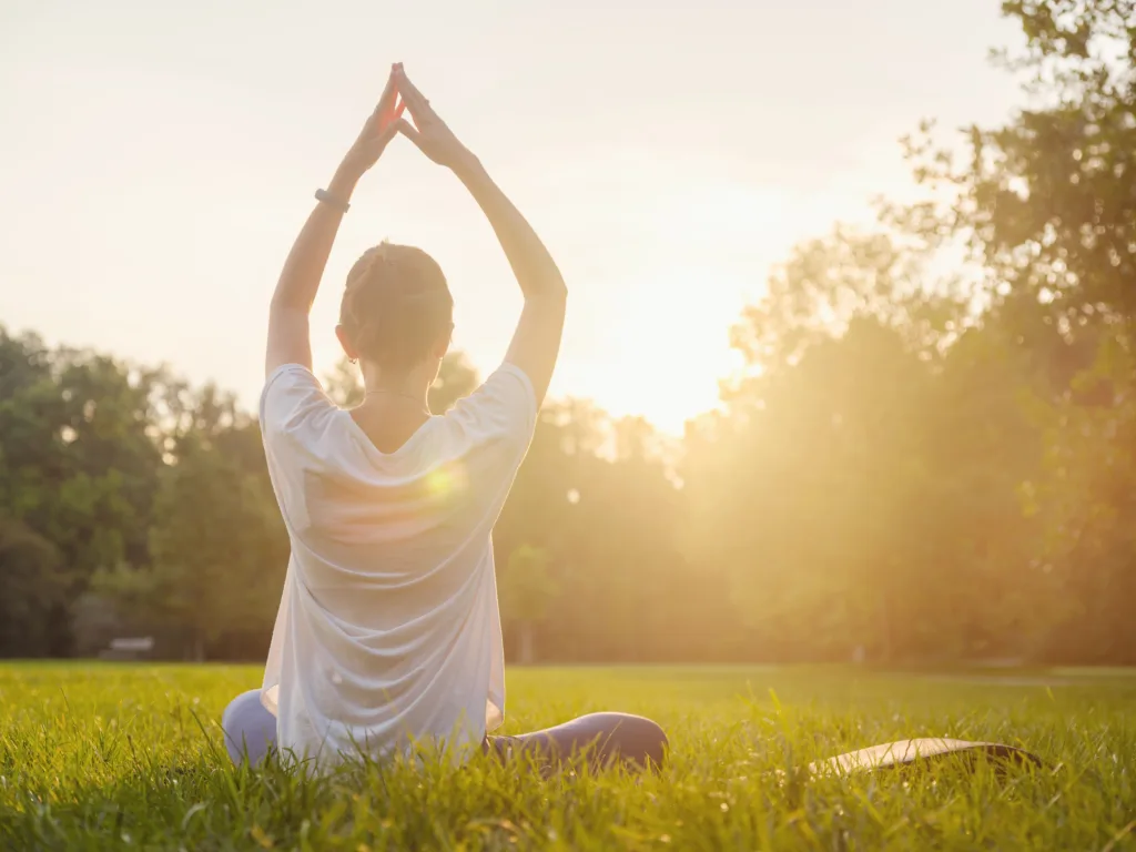 Woman sitting in the grass practicing yoga in the park.