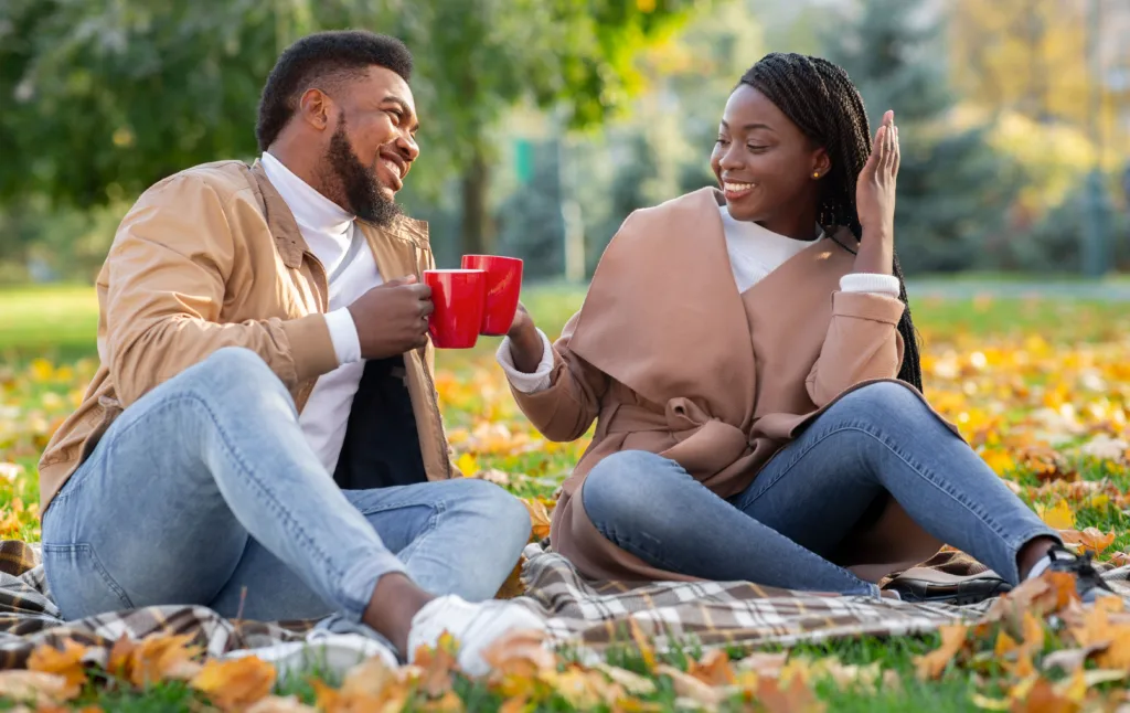 A man and woman are sitting on a blanket enjoying a picnic in the park.