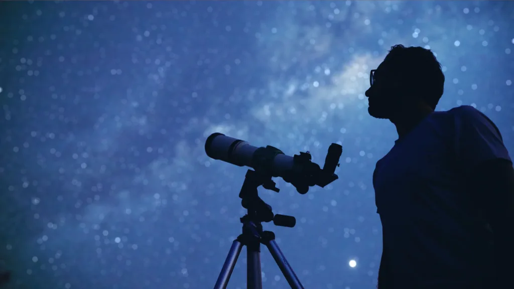 Man with a telescope looking up at a starry sky.