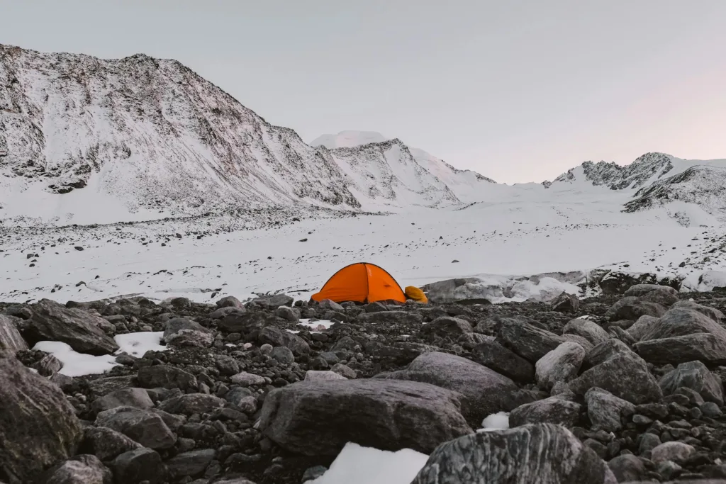 Orange camping tent set amidst a rocky, snow-capped mountain range, capturing serene nature.