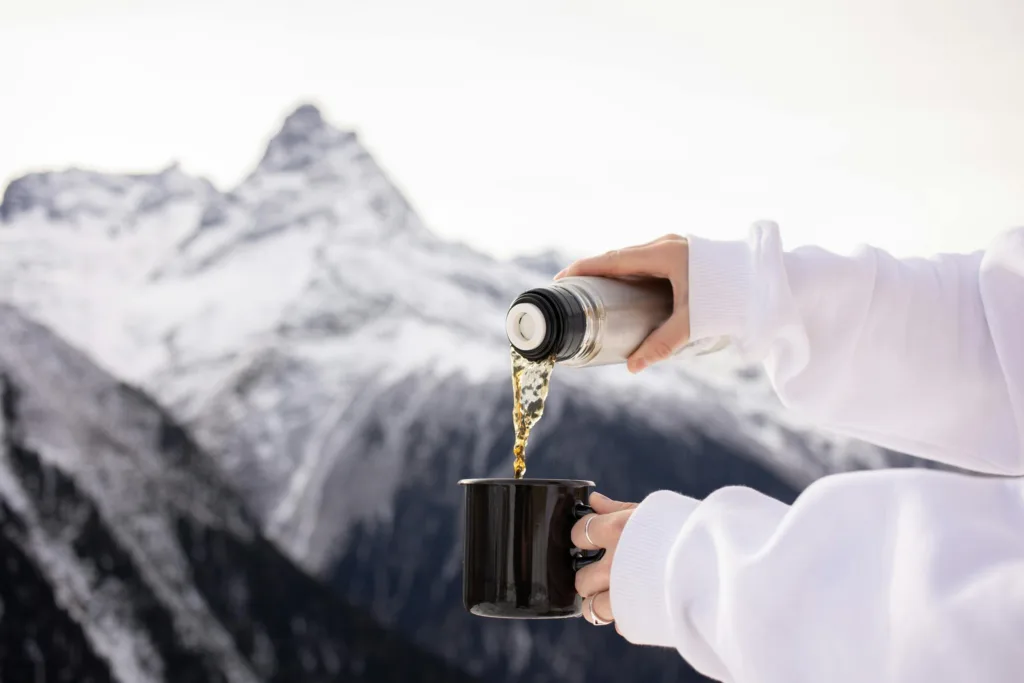 A hot beverage being poured into a mug against a snowy mountain backdrop.