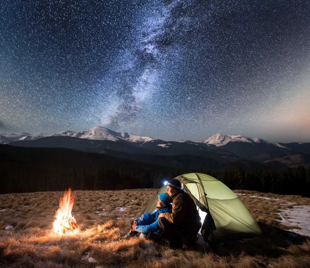 Couple tent camping, having a campfire and wearing headlamps.