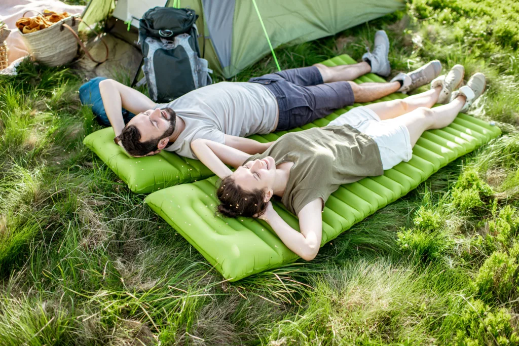 Couple lying on camping pads in the grass next to a tent.