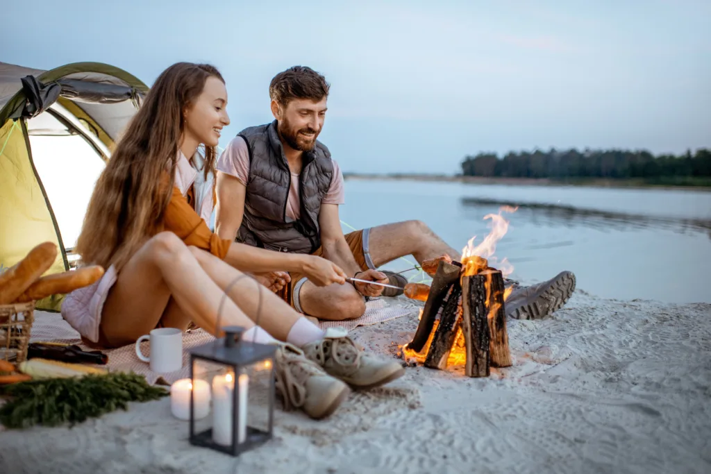 Young couple tent camping, having a campfire with a lantern nearby.