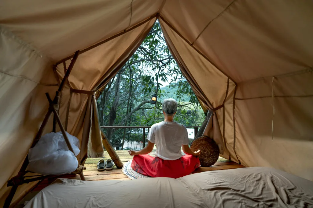 A woman meditates peacefully inside a tent, surrounded by nature's tranquility.