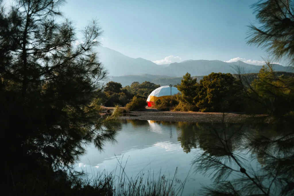 Peaceful geodesic dome by a forest lake with mountain views, ideal for nature retreats.