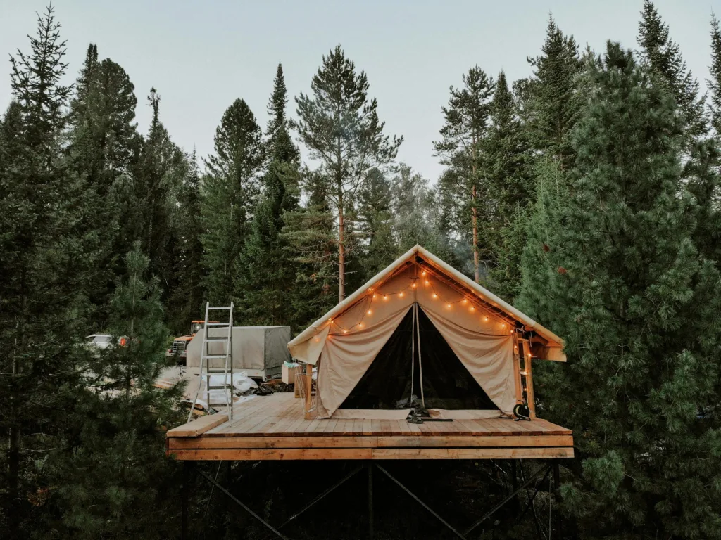 Campsite elevated in forest with fairy lights illuminating a cozy platform tent surrounded by lush trees.