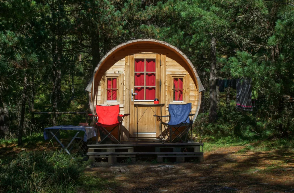Charming rustic wooden cabin in a tranquil forest with red and blue camping chairs.