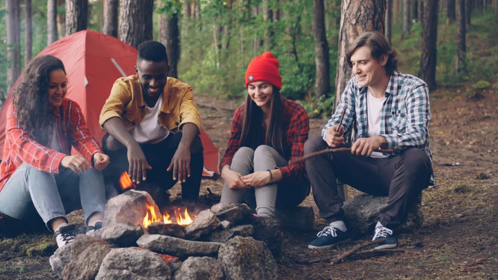 A group of friends gathered around a campfire in a serene forest setting.
