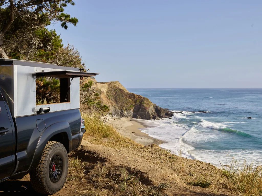 A serene coastal landscape featuring a pickup truck overlooking the beach and ocean waves under a clear sky.