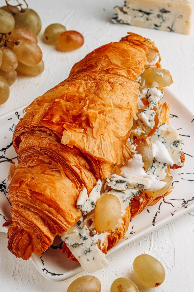 Delicious croissant with creamy blue cheese and fresh grapes on a plate.